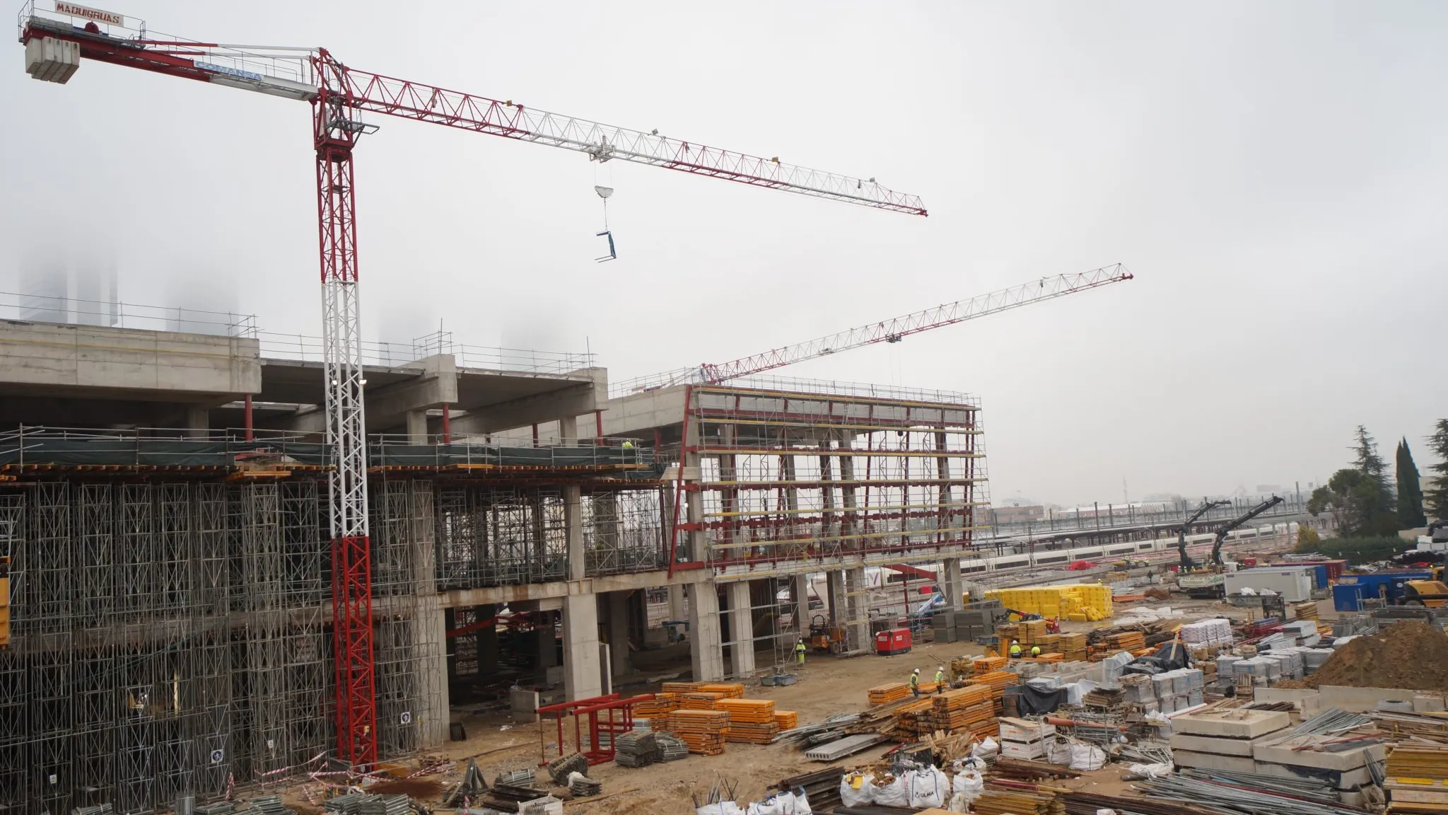 Immagine di contesto: cantiere edile di grandi dimensioni con gru e strutture in costruzione in una giornata di foschia.