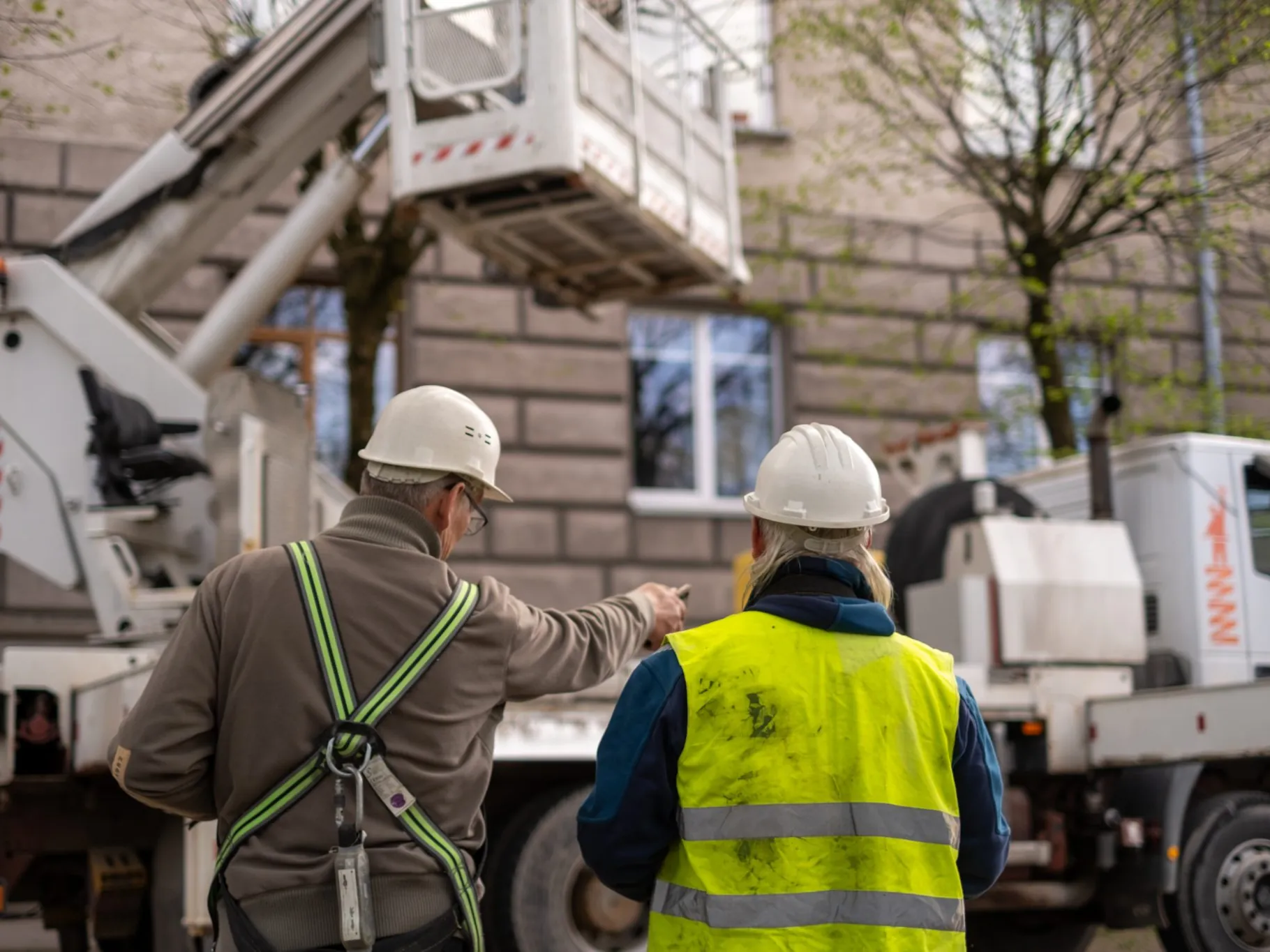 Immagine di contesto: due operatori al lavoro su una piattaforma elevabile davanti alla facciata di un edificio.